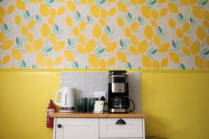 Eine Küche mit gelber Wand, einem gemusterten Wandpapier und einer Kaffeemaschine auf der Arbeitsfläche.