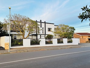A two-story building with a white facade, black window frames, and a black fence. - Designer Family Home with Garden & Workspace – Walking Distance to the Beach (Cape Town)