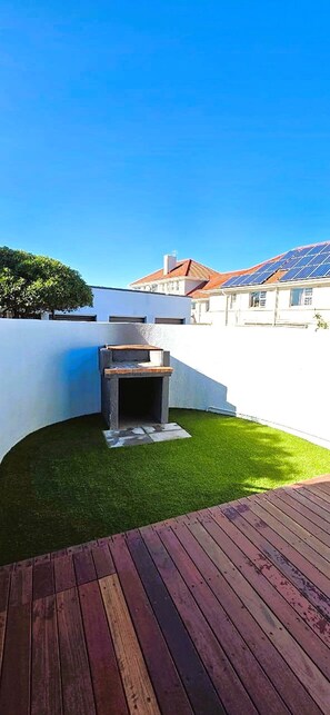 Ein Garten mit Grill, Kunstgrashalm und einer Holzterrasse.