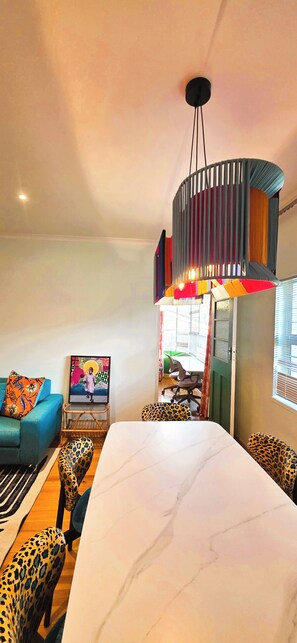 A modern living room with a large white marble table, leopard-print chairs, a blue sofa, and a unique hanging light fixture. - Designer Family Home with Garden & Workspace – Walking Distance to the Beach (Cape Town)