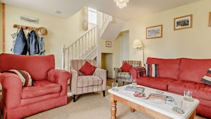A living room with a red sofa, striped armchair, and a coffee table with magazines and glasses. - 3 Bed in Fowey (oc-66074) (Polruan)