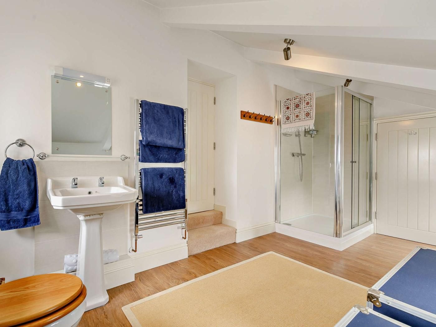 Une salle de bain équipée d’un lavabo, d’un miroir, d’un porte-serviettes, d’une douche et d’un revêtement de sol en bois.