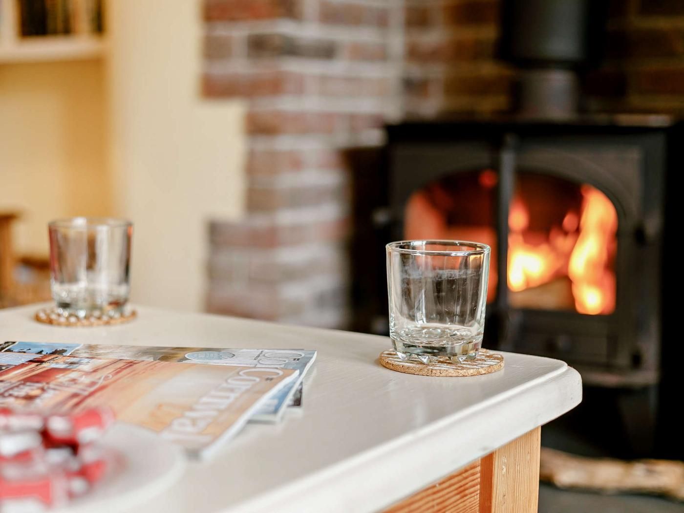 Une cheminée avec un feu visible, une table avec deux verres et un magazine posé sur la table.