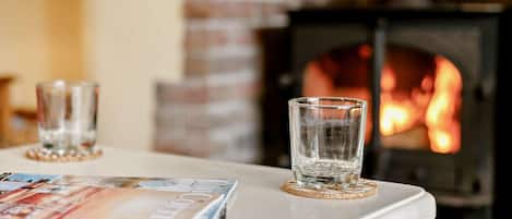A fireplace with a visible fire, a table with two glasses, and a magazine on the table.