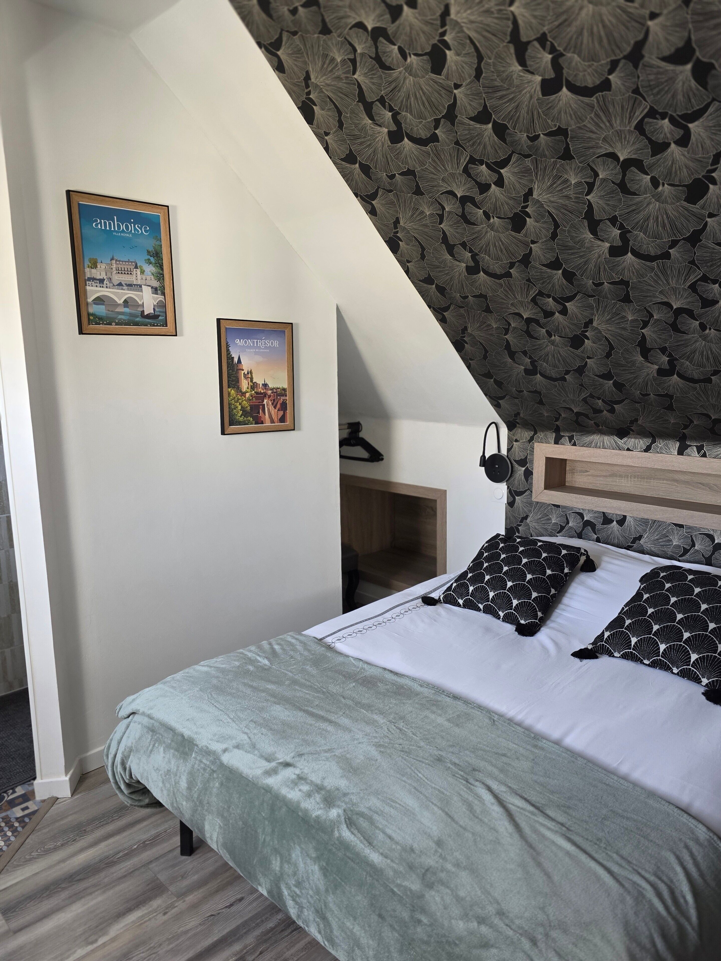 A bedroom with a bed, pillows, a headboard, a wall with a leaf pattern, and two framed pictures.