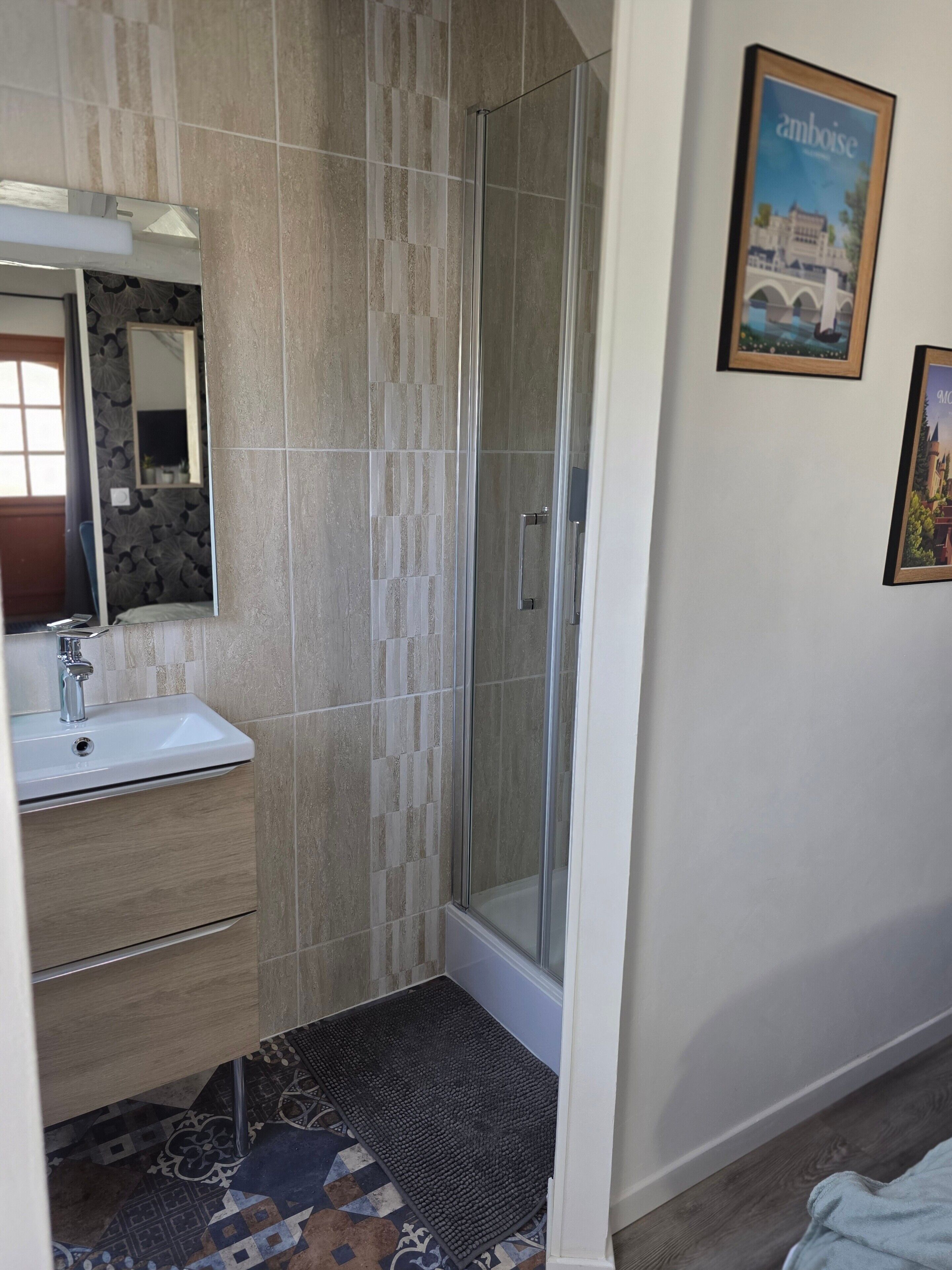 Un baño con ducha, lavabo, espejo y azulejos estampados.