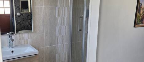 Un baño con ducha, lavabo, espejo y azulejos estampados.