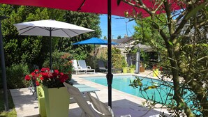 Zona junto a la piscina con sillones de descanso, sombrillas y plantas en macetas.