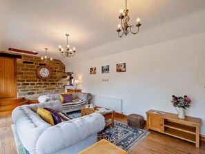 Ein gemütliches Wohnzimmer mit Steinwand, grauem Sofa, Holzschrank und einer Chandelier.