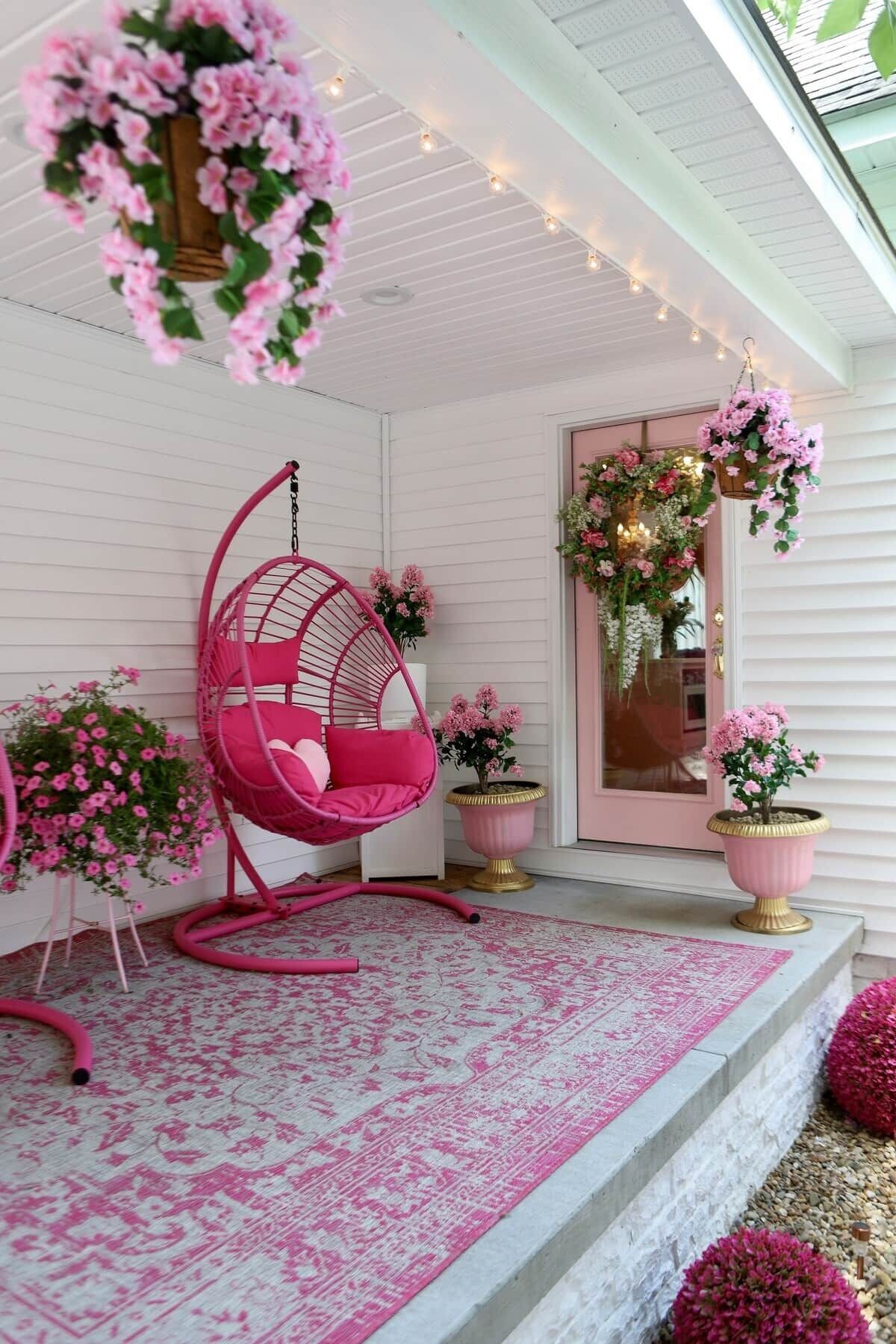 A porch with a hanging chair, potted plants, and a patterned rug.