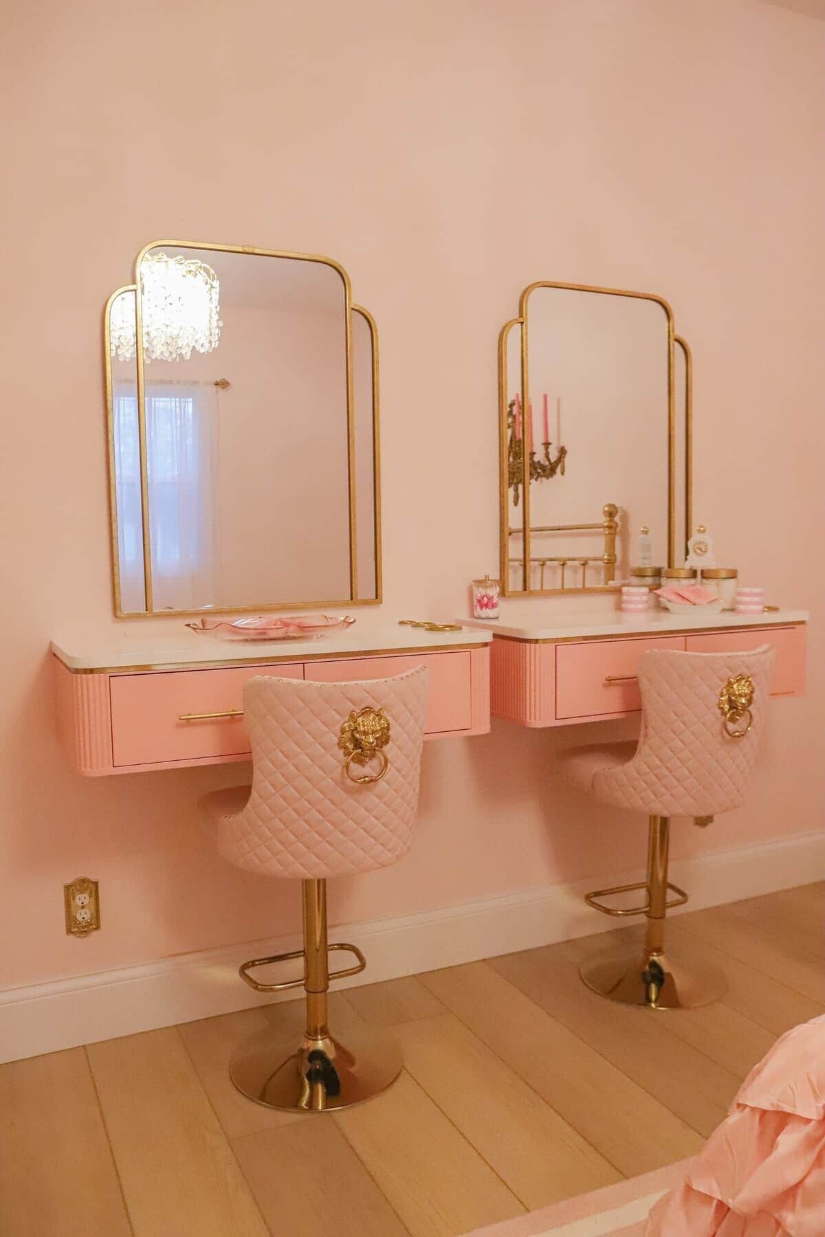 A pink vanity with two chairs, a mirror, and a vanity table with a gold frame.