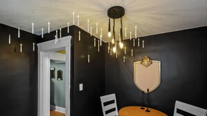 En matplats med ett runt träbord, vita stolar, en svart vägg och en taklampa.