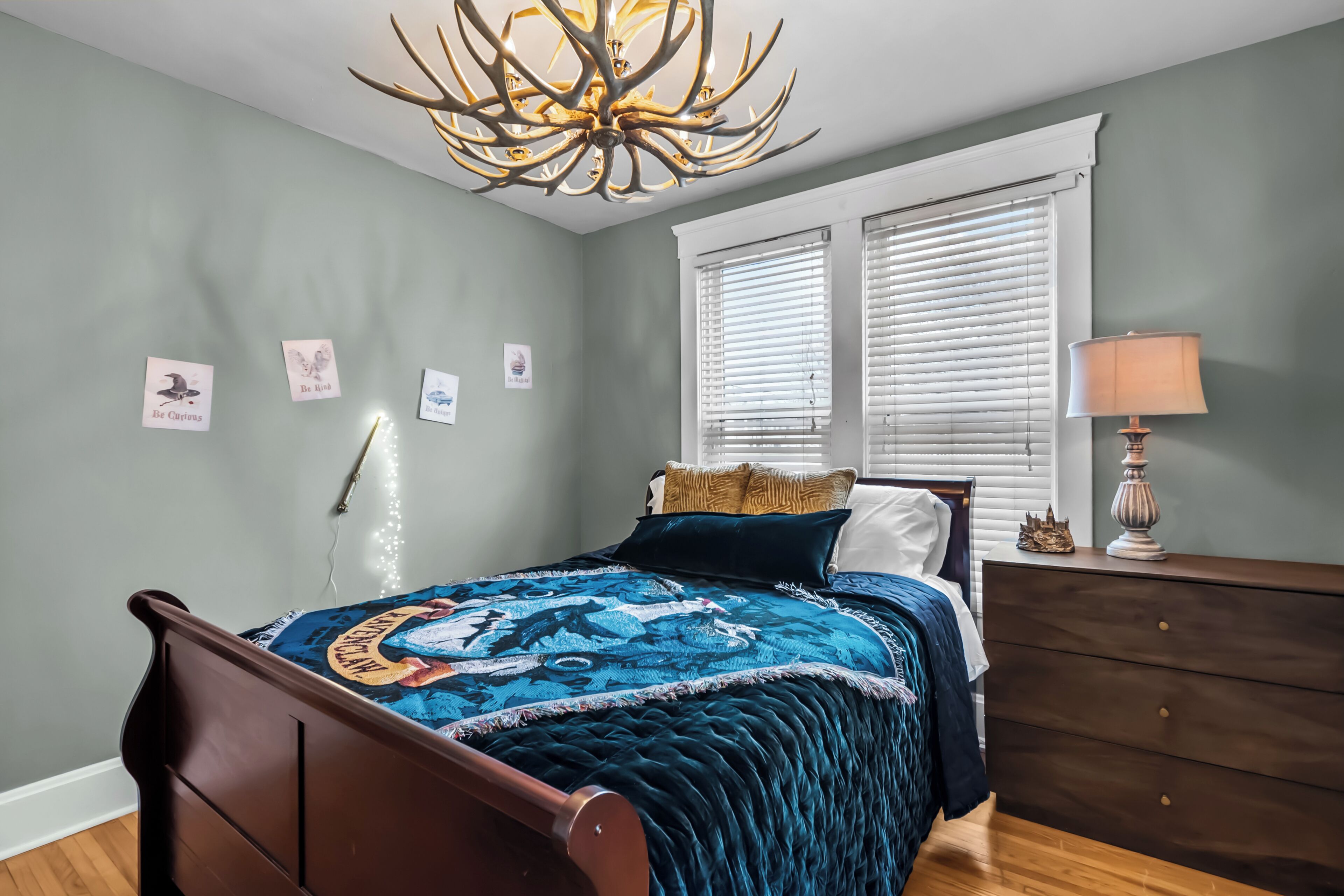 Un dormitorio con cama, candelabro, cómoda y ventana con persianas.