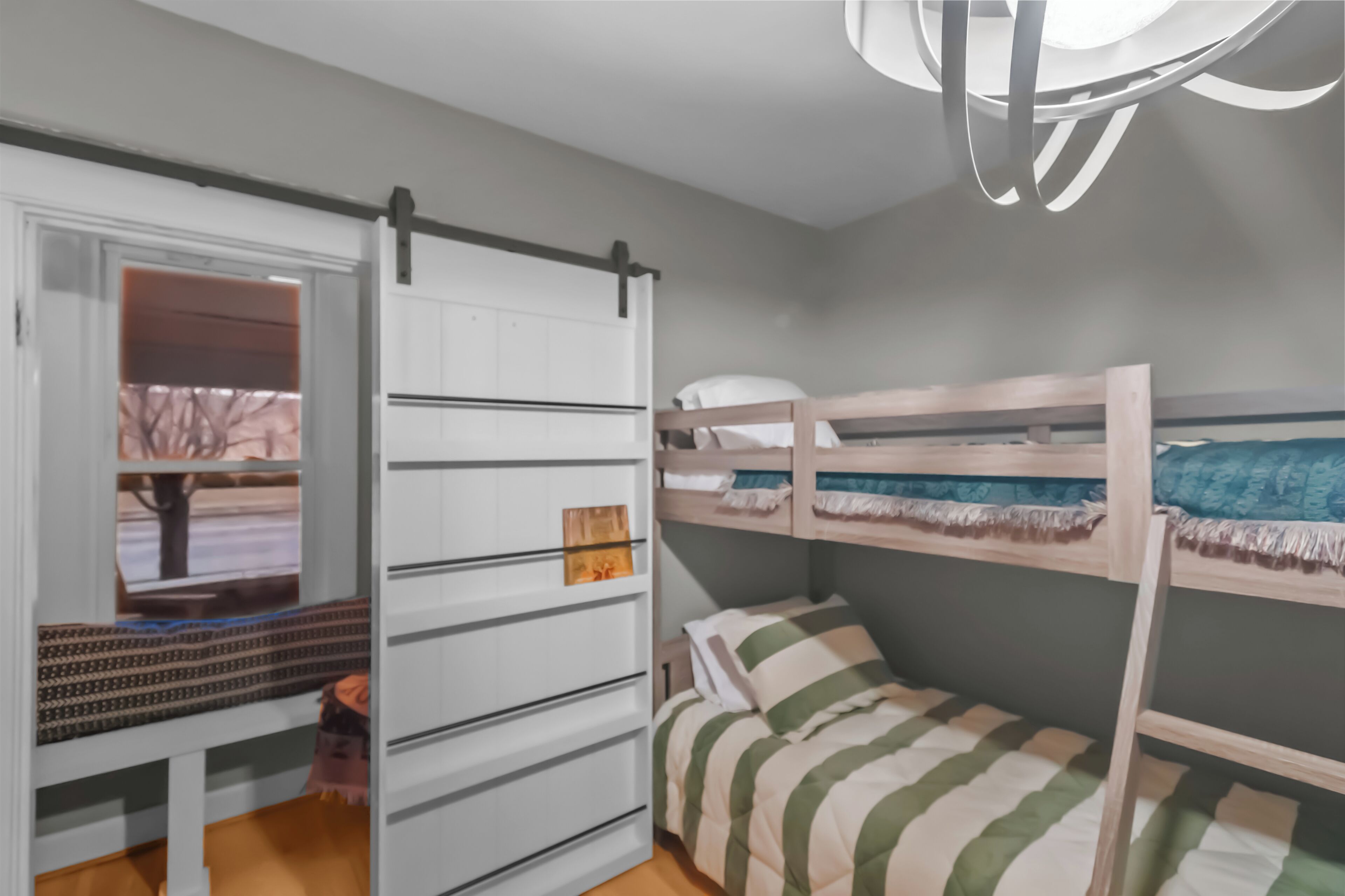 A bunk bed room with a sliding door closet, a window with a view, and a modern ceiling light fixture.
