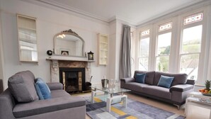 A living room with a fireplace, two sofas, a coffee table, and large windows. - 4 Bed in Ilfracombe (oc-66202) (Ilfracombe)