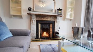 A living room with a fireplace, a sofa, a glass table, and a rug. - 4 Bed in Ilfracombe (oc-66202) (Ilfracombe)