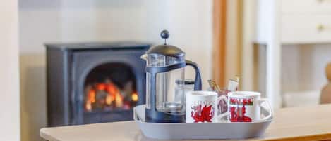 Uma cafeteira sobre uma bandeja com canecas em uma mesa em um quarto com lareira.