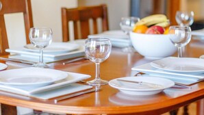 Een eettafel gedekt met borden, bestek en wijnglazen, met een fruitschaal op de achtergrond.