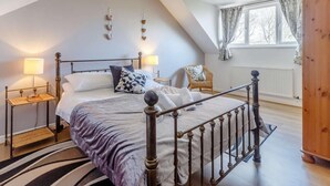 Een slaapkamer met een bed, twee nachtkastjes, een stoel, een raam met gordijnen en een houten kledingkast.