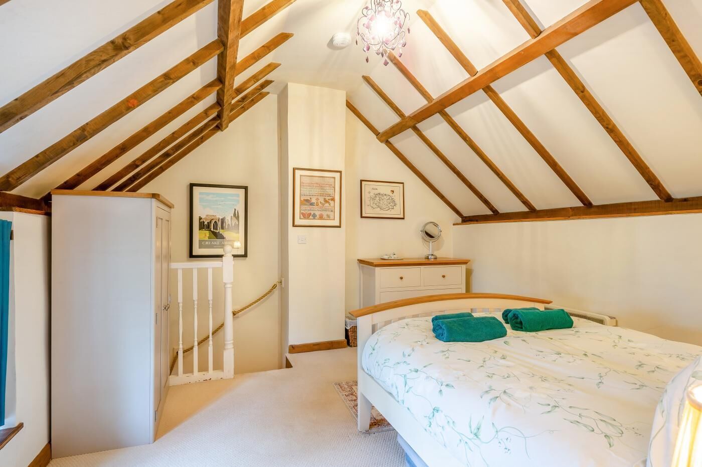 Quarto com teto inclinado, cama com toalhas verdes, cômoda e guarda-roupa branco.