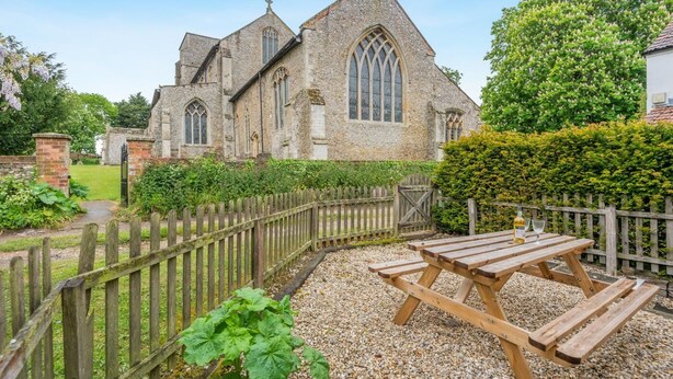 A stone church with a wooden fence and picnic table in the foreground. - 2 Bed in South Creake (oc-kt117) (South Creake)