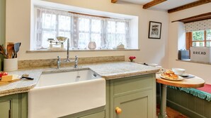 A kitchen with a sink, window with lace curtains, a 'BREAD' sign, and a table with food. - 2 Bed in South Creake (oc-kt117) (South Creake)