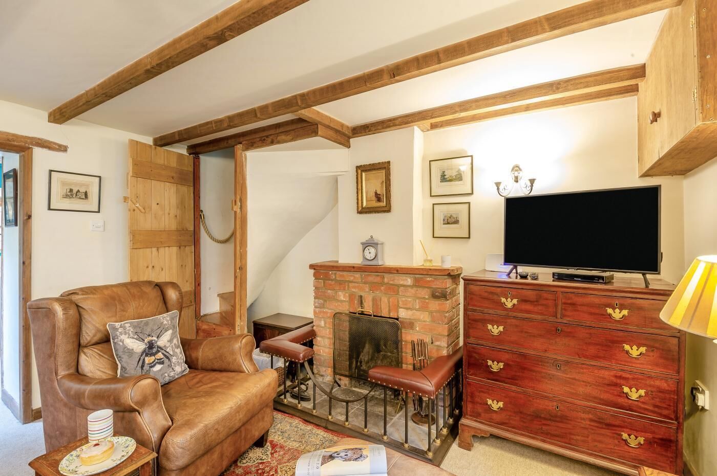 A cozy living room with a leather sofa, a brick fireplace, a wooden cabinet, and a television.