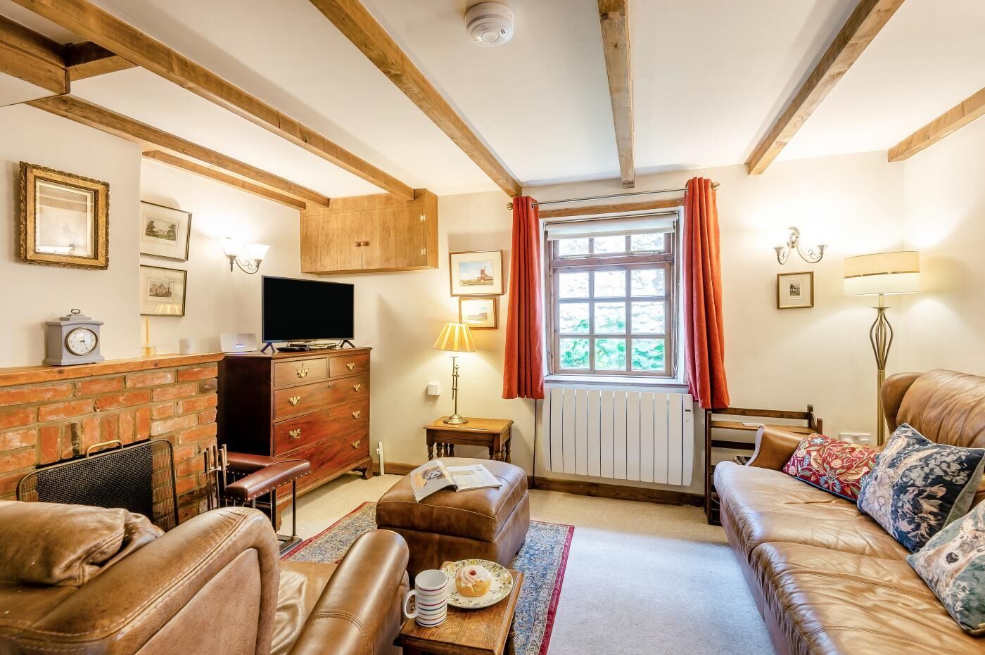 A cozy living room with a fireplace, leather sofas, a television, and a window with curtains.