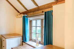 Ein Zimmer mit Ecke, Fenster, Holzbalken, einem kleinen Tisch und einem Schrank.