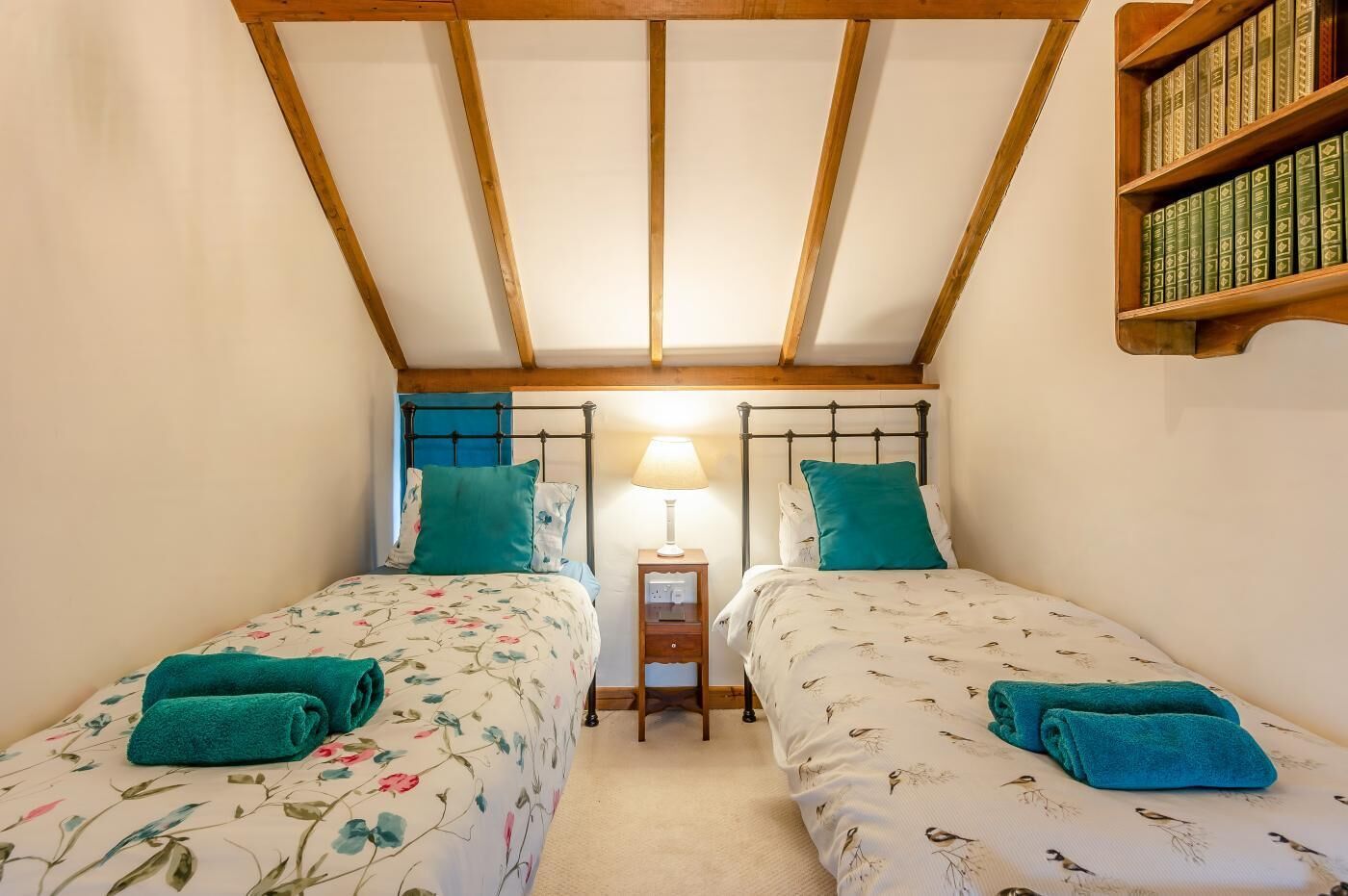 Une chambre avec deux lits simples, une table de chevet avec une lampe et une bibliothèque.
