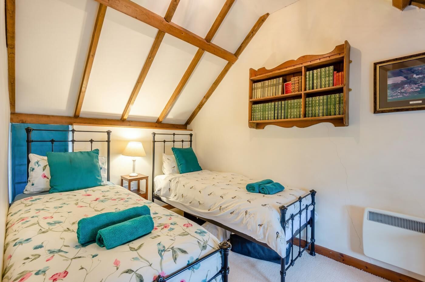 A bedroom with two beds, a bookshelf, a framed picture, and a radiator.