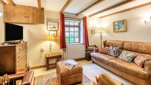 A cozy living room with a leather sofa, a wooden cabinet, a television, a lamp, and a window with curtains. - 2 Bed in South Creake (oc-kt117) (South Creake)