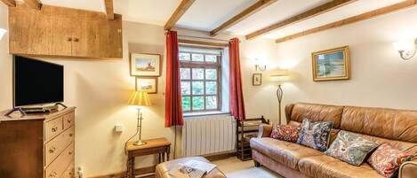 Ein gemütliches Wohnzimmer mit einer Ledersofa, einem Holzkasten, einem Fernseher, einer Lampe und einem Fenster mit Vorhängen.