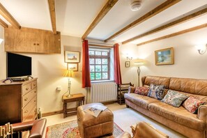 Ein gemütliches Wohnzimmer mit einer Ledersofa, einem Holzkasten, einem Fernseher, einer Lampe und einem Fenster mit Vorhängen.