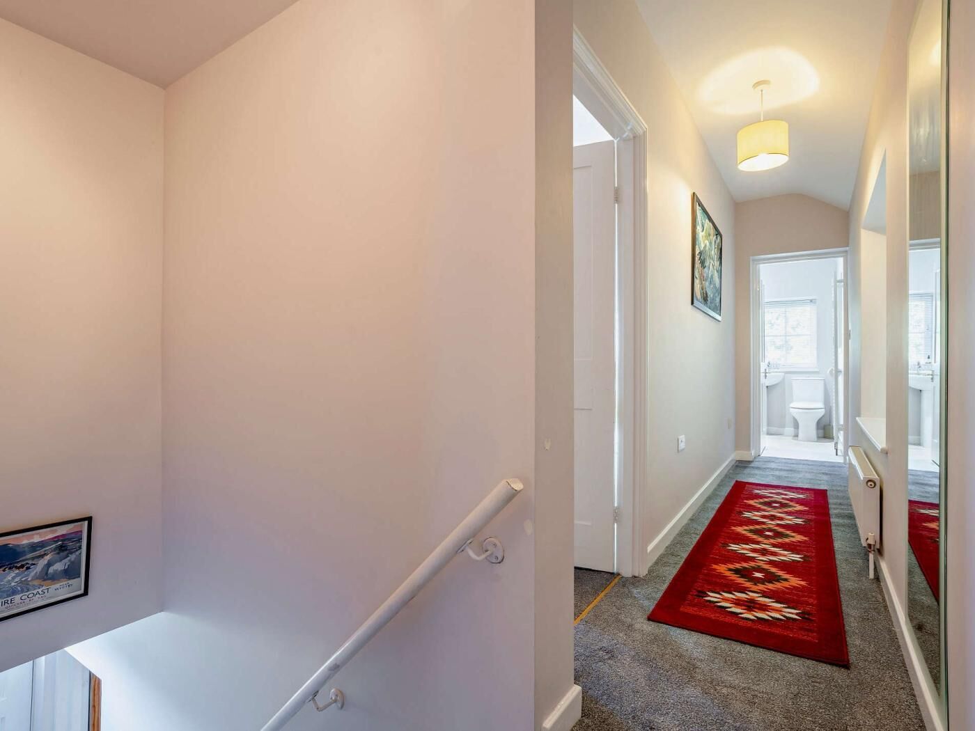 A hallway with a red carpet, white walls, and a door leading to a bathroom.
