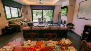 A dining area with a table set for breakfast, a sofa in the background, and a television mounted on the wall. - Villa La Huerta by Hacienda Alfacara (Benadalid)