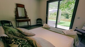 A bedroom with a large bed, a wooden dresser, a chair, and a view of the outdoors through a sliding door. - Villa La Huerta by Hacienda Alfacara (Benadalid)