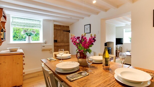 A dining area with a wooden table set for two, a vase of flowers, and a wine bottle. - 2 Bed in Syderstone (oc-kt197) (Syderstone)
