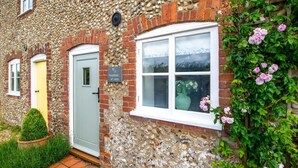 A stone house with a green door, a window with a white frame, and a garden with pink flowers. - 2 Bed in Syderstone (oc-kt197) (Syderstone)