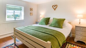 A bedroom with a bed, bedside lamps, a window with a view, a radiator, and a heart-shaped decoration on the wall. - 2 Bed in Syderstone (oc-kt197) (Syderstone)