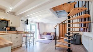 Une cuisine moderne avec un escalier en bois, un coin repas et un espace de vie comprenant un canapé et un téléviseur.