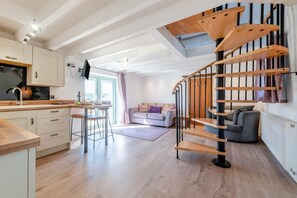 A modern kitchen with a wooden staircase, a dining area, and a living space with a sofa and a TV. - 1 Bed in Narberth (oc-72863) (Whitland)