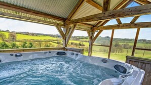 Un bain à remous avec une terrasse en bois et une vue sur des champs verdoyants.