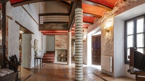 Een ruime binnenruimte met een hoge nok, zichtbare houten balken, een open haard en een stenen zuil.