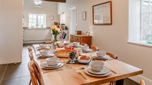 Ein Esszimmer mit Holztisch, gedeckt für eine Mahlzeit, im Hintergrund eine Küche und ein Fenster mit Blick.