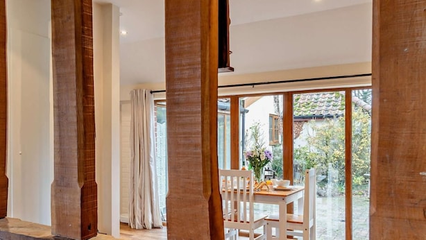 Una habitación con ventana de madera, una mesa de comedor con sillas y vista a un jardín.