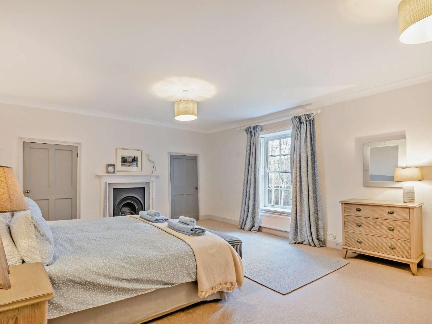 A bedroom with a bed, a fireplace, a dresser, a mirror, and a window with curtains.