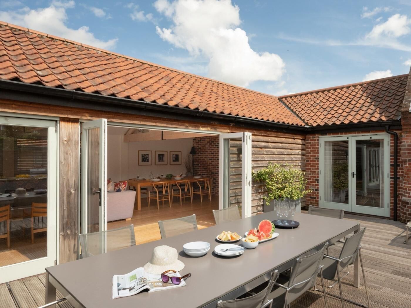 An outdoor dining area with a table set for two, a brick wall, and a glass door leading to a patio.