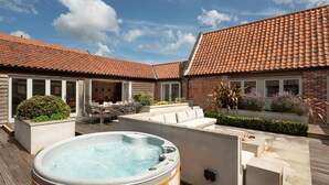 Een terras met een jacuzzi, tuinmeubilair en een gebouw met bakstenen muren en een pannendak.
