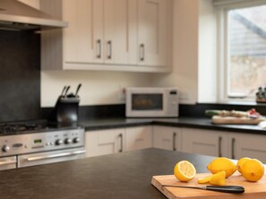 A kitchen with a microwave, stove, and a cutting board with lemons. - 4 Bed in Worstead (oc-65189) (Worstead)